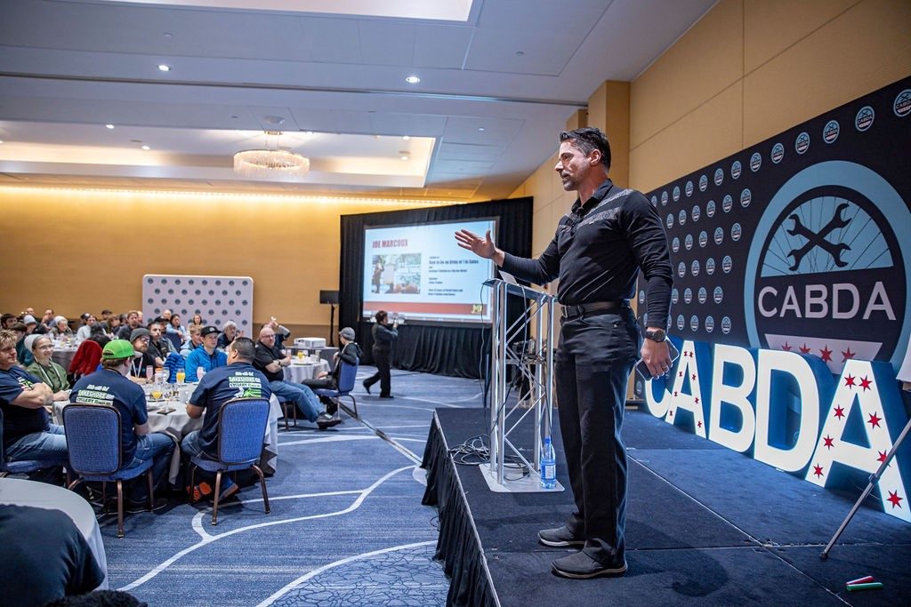 Joe Marcoux on stage at a CABDA keynote, gesturing in front of an audience